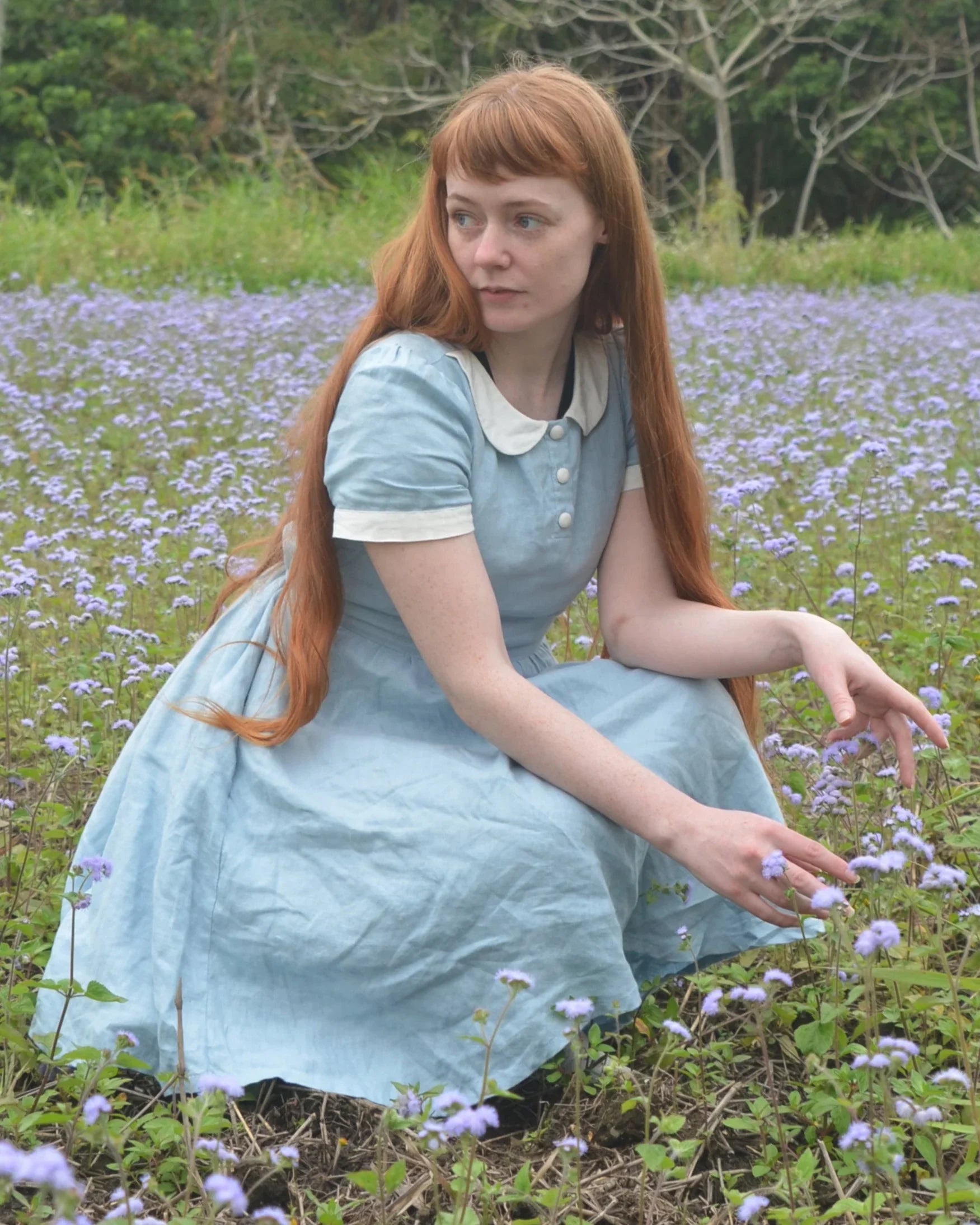 Woman in a blue linen dress sitting in a field of purple flowers